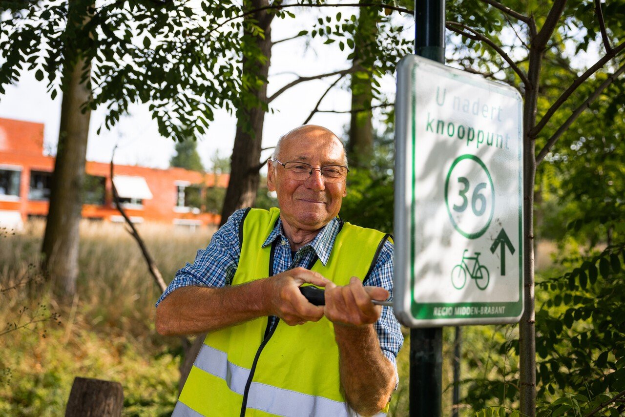 Man met gele veiligheidsvest plaatst fietsroutebord bij knooppunt 36 in regio Midden-Brabant.