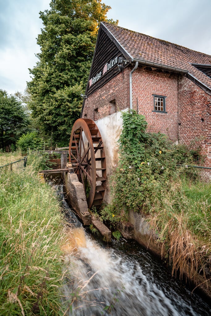 Watermolen met draaiend rad aan beek bij de Venbergse Molen in Valkenswaard, omgeven door groen in Brabant.