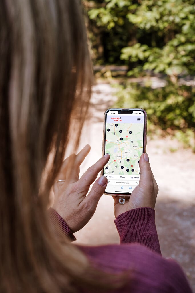 Vrouw gebruikt website op smartphone met kaart van wandelroutes in Brabant.