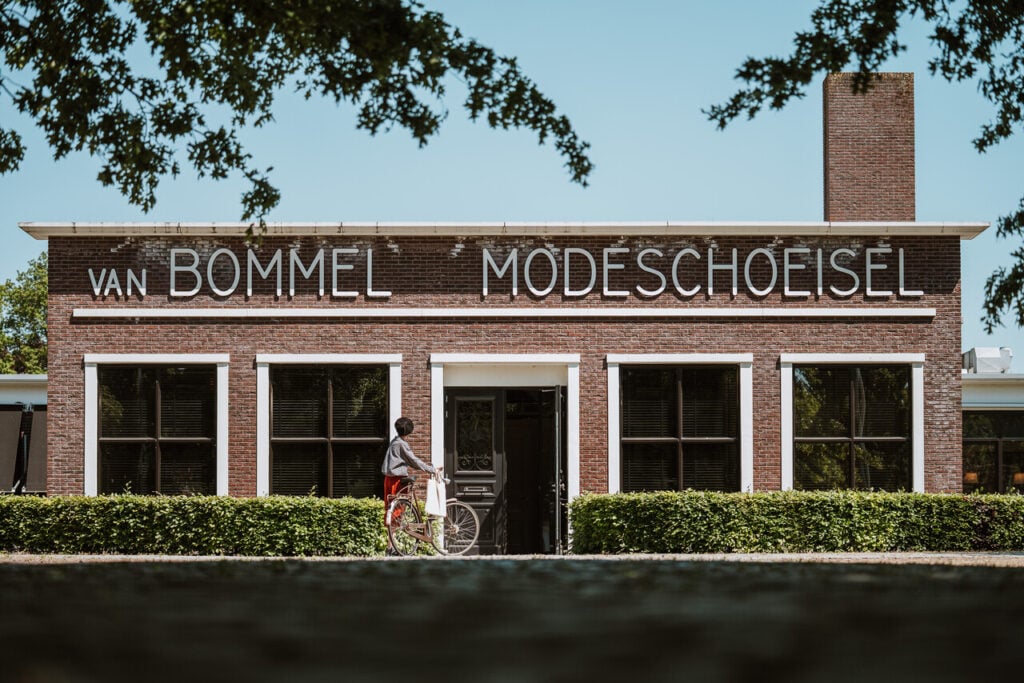 Persoon met fiets voor historische gevel van Van Bommel Modeschoeisel in Brabant.