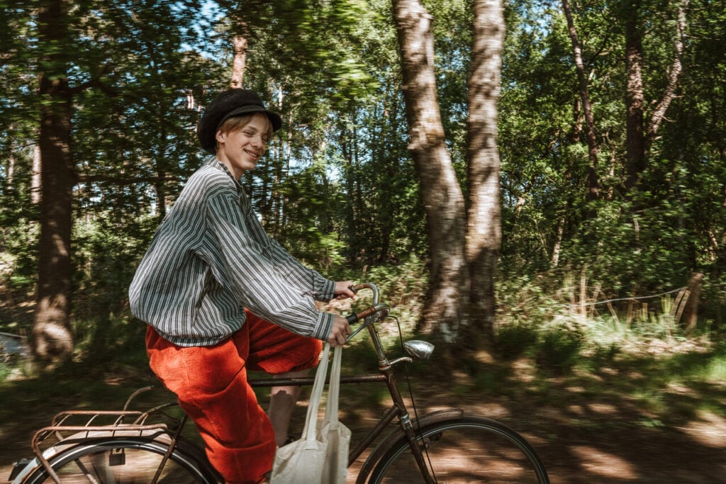 Jongen fietst door groen bos met zonlicht in Brabant, gekleed in rood en gestreept overhemd.