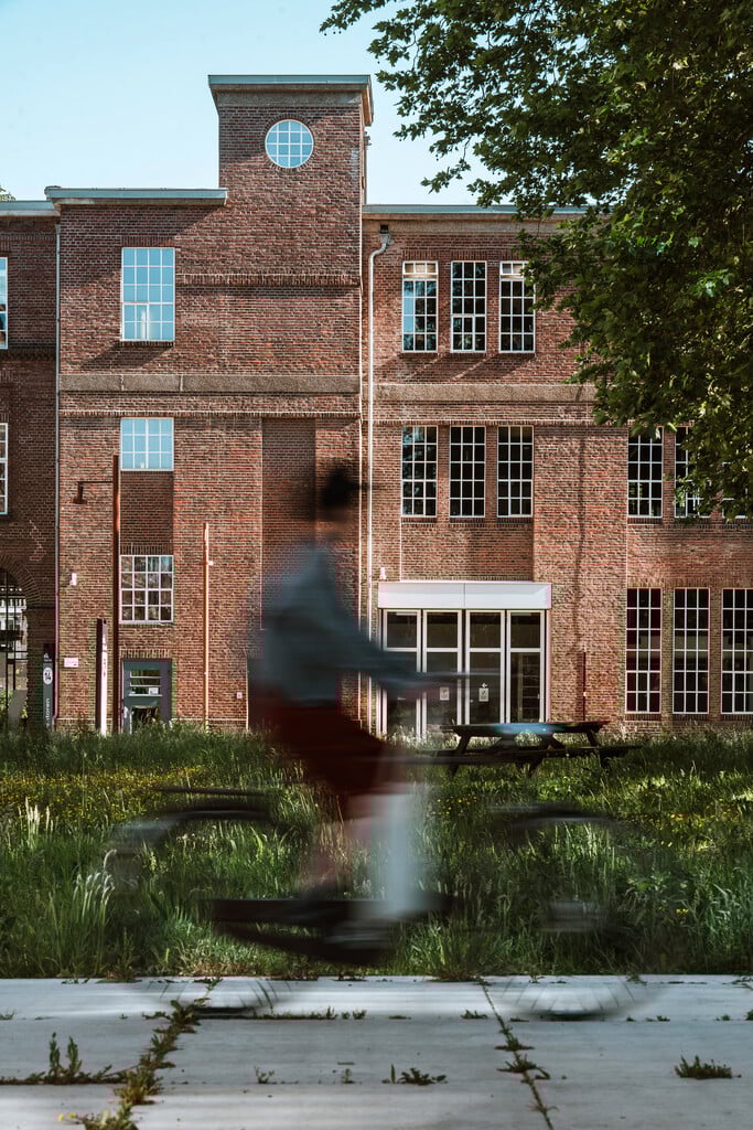 Een fietser rijdt via themaroute voorbij een karakteristiek fabriekspand met hoge ramen in Brabant.