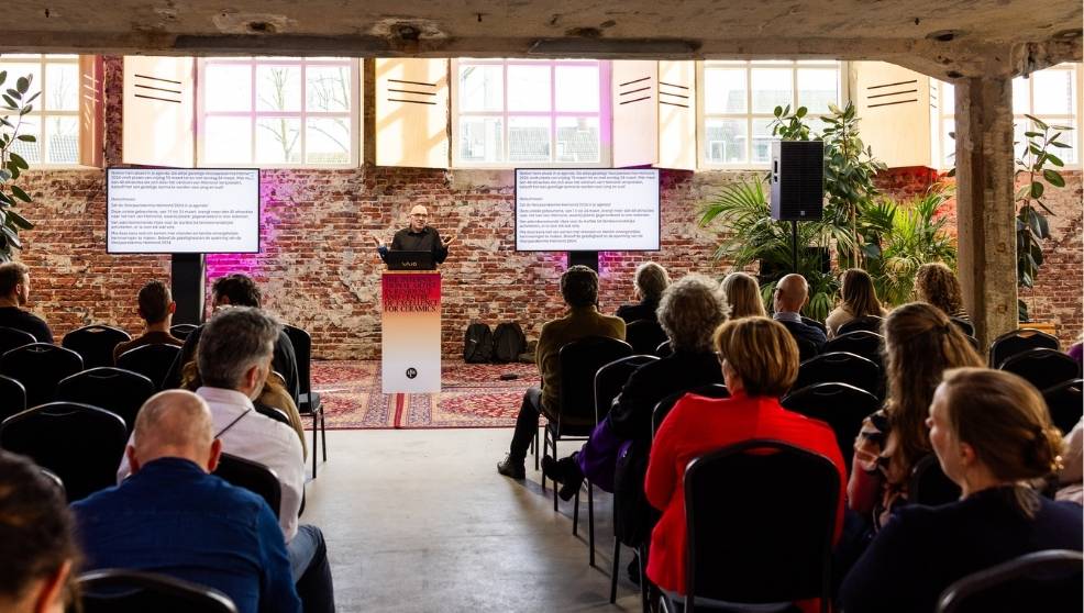 Mensen luisteren naar spreker tijdens partnerevent in sfeervolle industriële zaal met bakstenen muren.