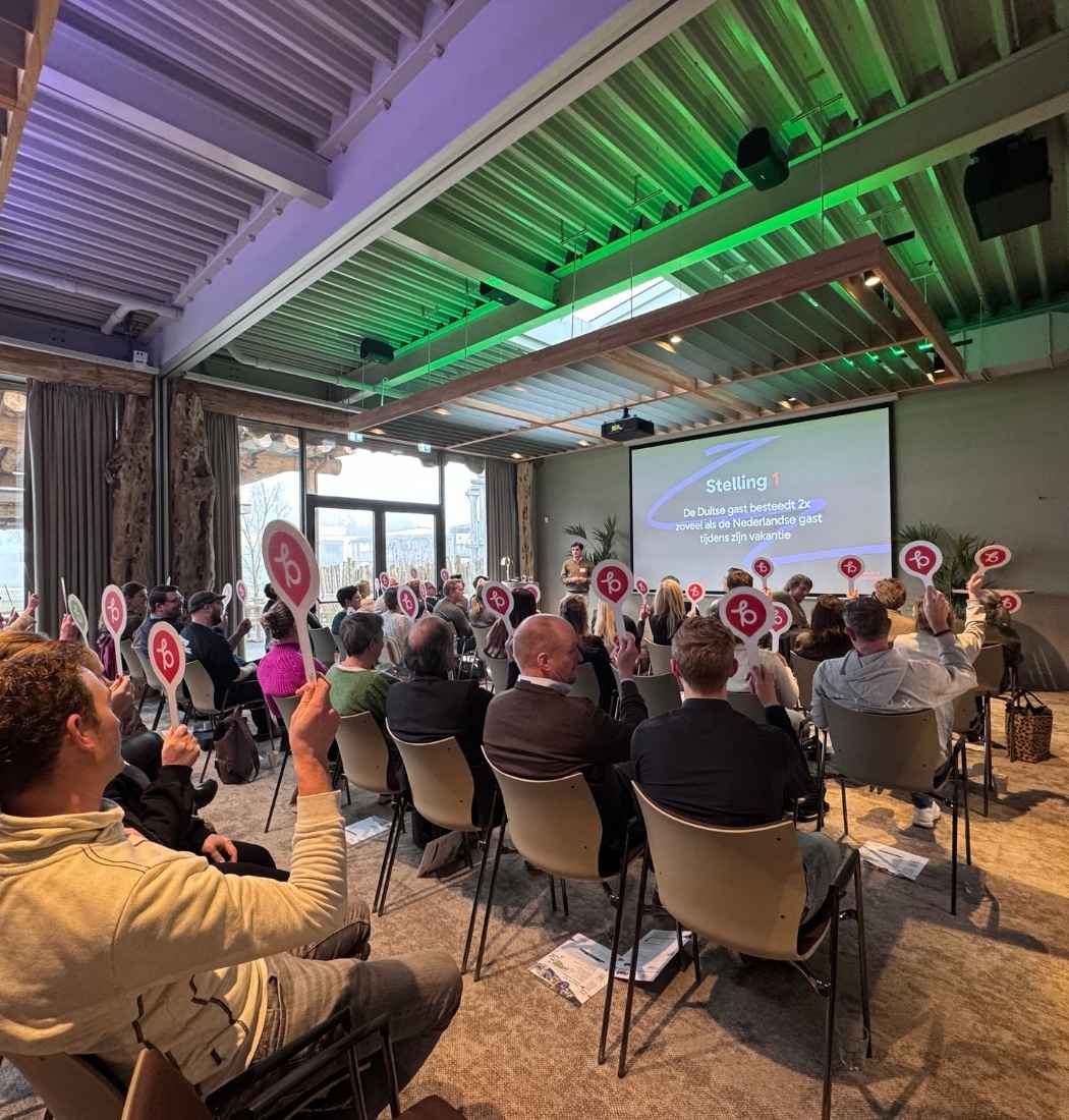 Publiek stemt met bordjes tijdens interactieve presentatie over internationale gastvrijheid met ondernemers uit Hart van Brabant in een zaal van Beekse Bergen, Brabant.