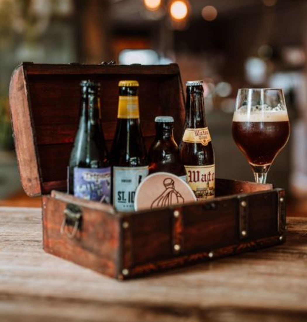 Smokkelkistje met Brabantse speciaalbieren en glas op houten tafel, onderdeel van de smokkelroute in De Groote Heide.